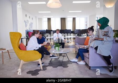 Multiethnic startup business team having brainstorming in relaxation area of modern office interior working on laptop and tablet computer Stock Photo