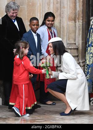 Meghan Markle, wearing a cream Amanda Wakeley coat and matching hat, receives a posy of flowers from a young girl following the Commonwealth Service at Westminster Abbey in London on March 12, 2018. Stock Photo