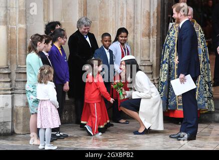 Prince Harry and Meghan Markle, wearing a cream Amanda Wakeley coat and matching hat, receive posies from a young girl following the Commonwealth Service at Westminster Abbey in London on March 12, 2018. Stock Photo