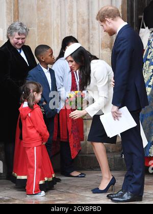 Prince Harry and Meghan Markle, wearing a cream Amanda Wakeley coat and matching hat, receive posies from a young girl following the Commonwealth Service at Westminster Abbey in London on March 12, 2018. Stock Photo