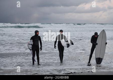 Authentic local Arctic surfers going by snowy beach after surfing in Northern sea. Norwegian sea coastline. Winter water activities extreme sport Stock Photo