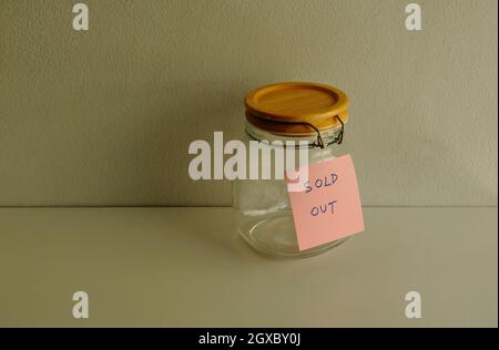Selective focus on adhesive note with message sold out attached to a jar placed on wooden table against cement wall Stock Photo