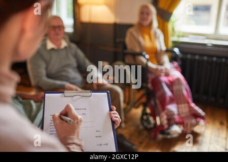 Close up of young woman writing on clipboard during therapy session at retirement home, copy space Stock Photo