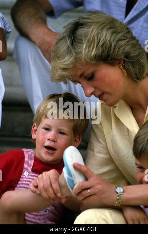 Princess Diana, Princess of Wales helps Prince Harry put on his shoes whilst on holiday in Majorca, Spain on August 10, 1987. Also present were the Spanish Royal Family and Prince Charles, Prince of Wales. Stock Photo