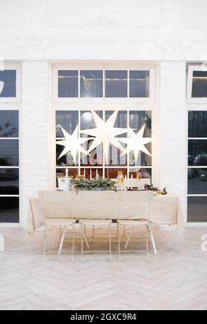 A cozy festive table for celebrating Christmas or New Year in a classic style. Chandeliers in the form of stars hang above the table Stock Photo