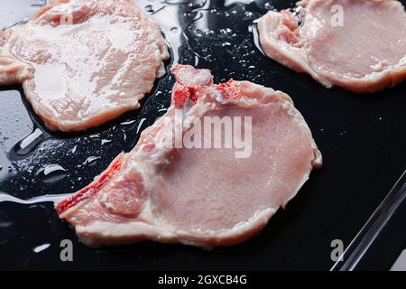 Raw pork chops on black baking tray seasoned with oil and ready for barbecue Stock Photo