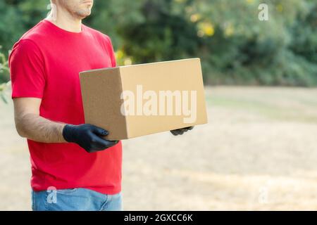 Delivery man holding cardboard boxes on the farm in medical gloves. Express delivery Courier order online shopping concept Organic food  Stock Photo
