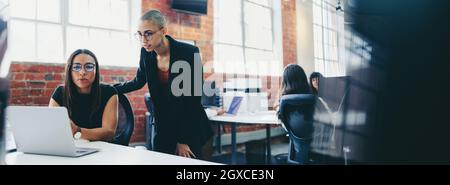 Two young businesswomen working together in a creative office. Female colleagues using a laptop together while working on a new project. businesswomen Stock Photo