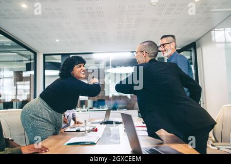 Cheerful businesswomen elbow bumping each other before a meeting in a boardroom. Group of businesspeople attending a briefing in a modern workplace. M Stock Photo