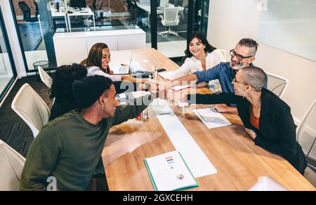 Group of happy businesspeople bringing their fists together while sitting in a boardroom. Diverse group of colleagues smiling cheerfully during a meet Stock Photo