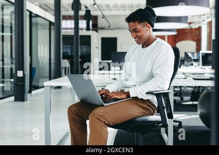 Happy young businessman working on a new project in the office. Creative businessman smiling cheerfully while using a laptop in a modern workplace. Yo Stock Photo