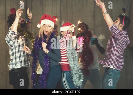 multiethnic group of young happy casual business people dancing with sparklers and having fun while celebrating new year eve in front of concrete wall Stock Photo