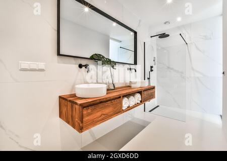 Creative design of bathroom with double counter washstands under mirror reflecting lamps and shower cabin with glass walls in house Stock Photo