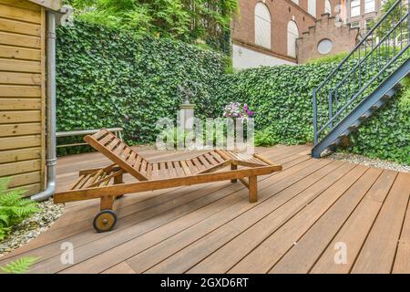 Comfortable deckchair placed on wooden terrace of cottage near green hedge in countryside in summer Stock Photo