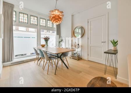 Modern interior of dining room with wooden table and plastic chairs under creative chandelier in spacious new flat Stock Photo