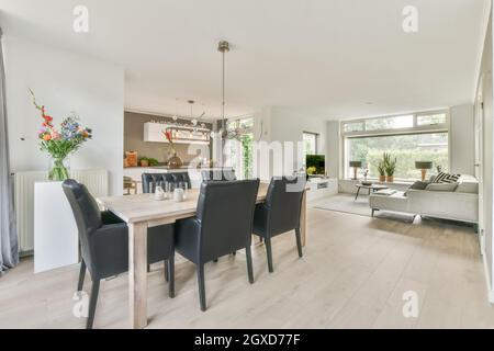 Wooden table and black leather chairs in spacious light dining room near large comfortable sofa placed in modern house Stock Photo