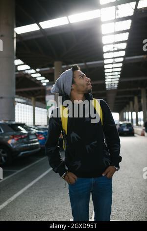 Stylish African American male hipster with backpack and in hoodie standing on underground parking in city Stock Photo