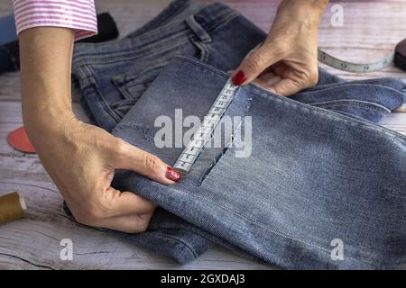 From above of crop anonymous female dressmaker using measuring tape while sewing jeans in atelier in daytime Stock Photo