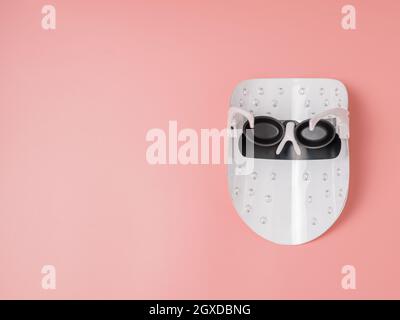 Led light therapy facial mask on pink background. Home skincare and me time concept. Light rejuvenating mask for facial skin therapy. Photodynamic the Stock Photo