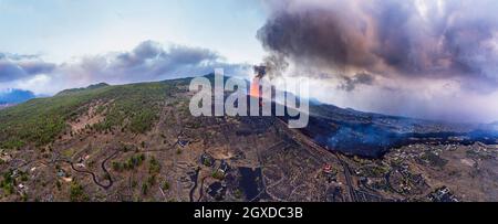 Aerial view of the hot lava and magma pouring out of the crater with plumes of smoke near the town houses. Cumbre Vieja volcanic eruption in La Palma Stock Photo