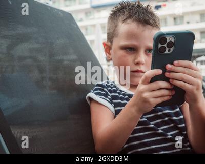 Serious boy in t shirt lying alone and browsing Internet on modern mobile phone Stock Photo