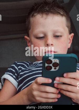 Serious boy in t shirt lying alone and browsing Internet on modern mobile phone Stock Photo