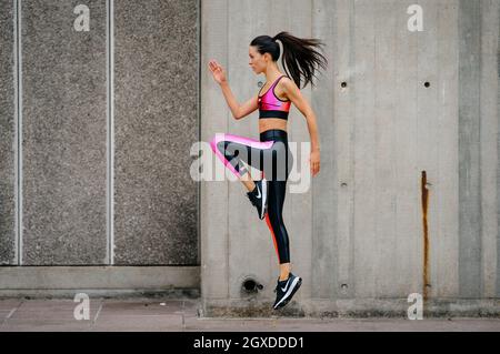 An athletic woman in a pink sports outfit jumping in an urban environment Stock Photo