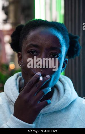 Thoughtful African American non binary female in casual hoodie smoking cigarette and looking away pensively Stock Photo