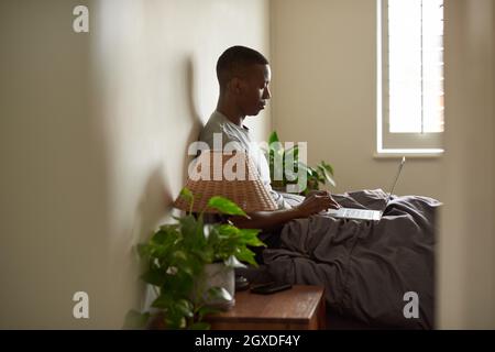 Young African man using at laptop in bed in the morning Stock Photo
