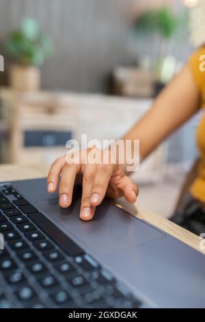 Cropped unrecognizable young female entrepreneur sitting at table and browsing netbook while working on modern workplace Stock Photo