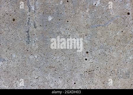 A flat grey concrete surface. The surface is textured and covered in holes from lots of tiny air bubbles. Stock Photo