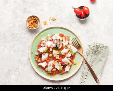 Summery tomato and cod salad in a shallow dish with a fork and a bowl of fried onions Stock Photo
