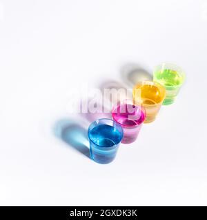 Plastic multi-colored glasses with liquid on a white background with highlights. Layout, mockup. Stock Photo