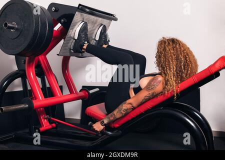 Side view of unrecognizable sportsWoman with curly hair doing exercises on leg press machine in gym Stock Photo