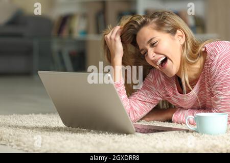 Funny woman laughing loud watching media on laptop lying on the floor at home Stock Photo