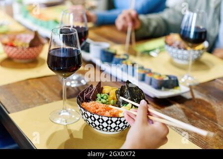 Person enjoying a bowl of poke or marinated seasoned raw fish with a glass of red wine in a restaurant with friends in a close up on the food Stock Photo
