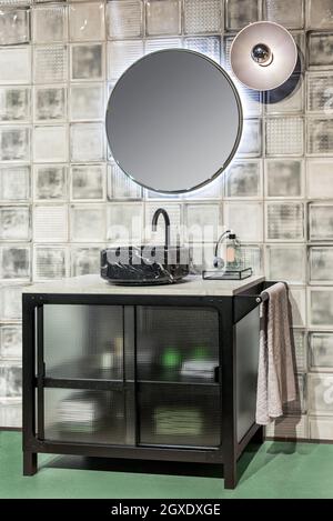 Contemporary interior of bathroom with black marble sink and illuminated round shaped mirror hanging on tiled wall Stock Photo