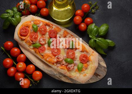 Flatbread pizza garnished with fresh cherry tomatoes,basil,cheese and olive oil on wooden pizza board. Dark background Stock Photo