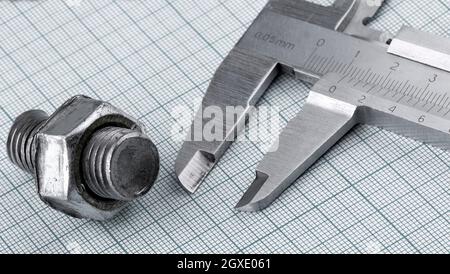 The bolt with nut and caliper on engineering paper. Close up Stock Photo
