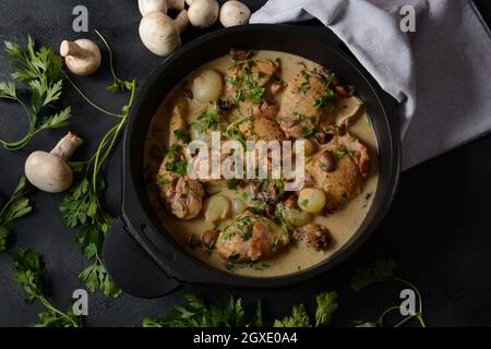 Fricassee - French Cuisine. Chicken stewed in a creamy sauce with mushrooms in a black dutch oven on a black table Stock Photo