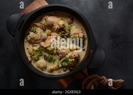 Fricassee - French Cuisine. Chicken stewed in a creamy sauce with mushrooms in a black dutch oven on a black table Stock Photo