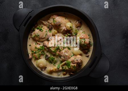 Fricassee - French Cuisine. Chicken stewed in a creamy sauce with mushrooms in a black dutch oven on a black table Stock Photo