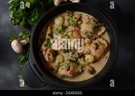 Fricassee - French Cuisine. Chicken stewed in a creamy sauce with mushrooms in a black dutch oven on a black table Stock Photo