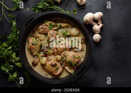 Fricassee - French Cuisine. Chicken stewed in a creamy sauce with mushrooms in a black dutch oven on a black table Stock Photo