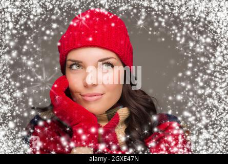 Happy Mixed Race Woman Wearing Winter Hat and Gloves Enjoys Watching the Snow Fall Looking to the Side on Gray Background. Stock Photo