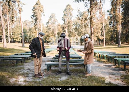 Multiethnic senior friends with smartphone and walking cane using vr headsets in autumn park Stock Photo