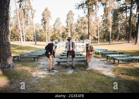 Smiling elderly man using vr headset near multicultural friends in park in autumn Stock Photo