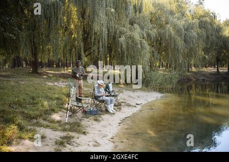 Cheerful multicultural men in fishing outfit holding thermo cups near lake  Stock Photo - Alamy