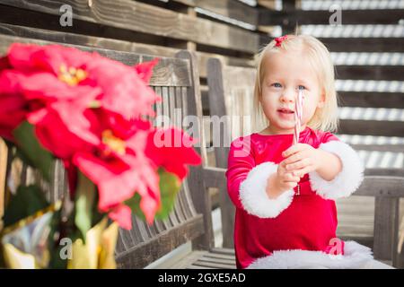 Adorable Little Girl Sitting On A Bench with Her Candy Cane Outside. Stock Photo