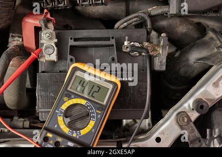 Car starter battery voltage measured with multimeter. Voltage above 14 volts as the alternator is charging the battery. Electric system working well. Stock Photo